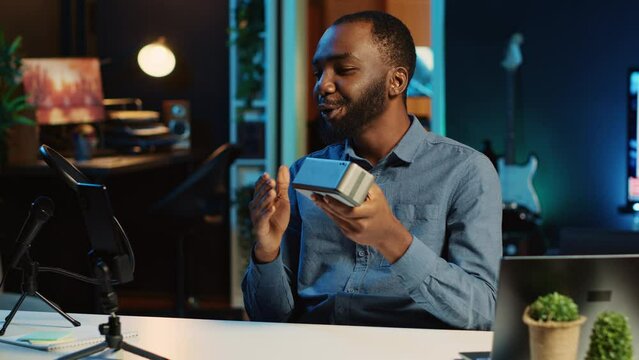 African american internet star doing technology review of Bluetooth portable speaker for online platforms channel. BIPOC influencer presenting music playing device to his viewership