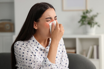 Fototapeta na wymiar Suffering from allergy. Young woman blowing her nose in tissue at home