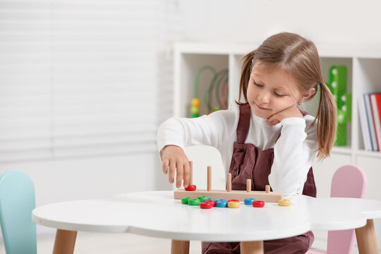 Cute little girl playing with stacking and counting game at white table indoors, space for text. Child's toy