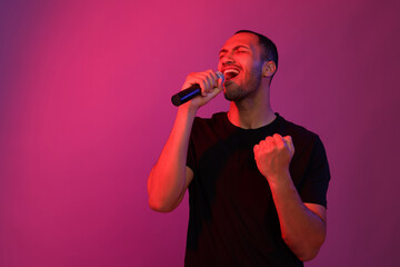 Handsome man with microphone singing on pink background, space for text. Color tone effect