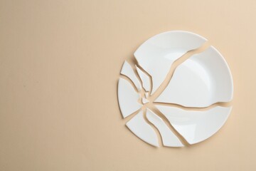 Pieces of broken ceramic plate on beige background, flat lay. Space for text