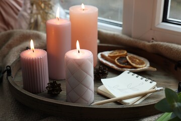 Fototapeta na wymiar Tray with burning wax candles and decor on window sill indoors