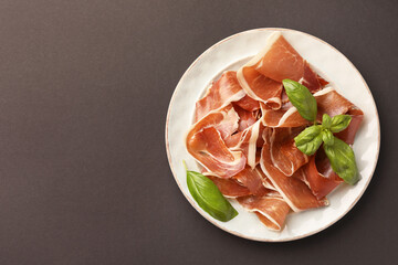 Slices of tasty cured ham and basil on grey background, top view. Space for text