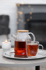 Teapot, cup of aromatic tea and burning candle on white table indoors, space for text