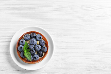 Tartlet with fresh blueberries on white wooden table, top view and space for text. Delicious dessert