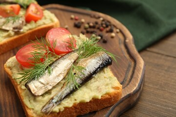 Delicious sandwich with sprats, tomato, dill and avocado puree on wooden table, closeup. Space for text