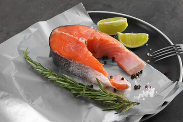 Aluminum foil with raw fish, lime, rosemary and spices on grey table, closeup. Baking salmon