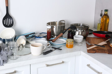 Many dirty utensils, cookware and dishware on countertop in messy kitchen