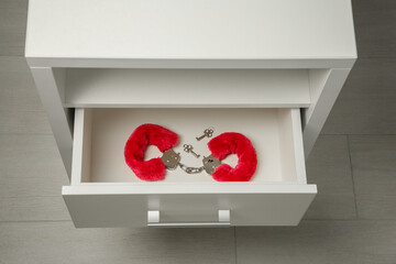 Red furry handcuffs and keys in drawer indoors, above view. Sex toy