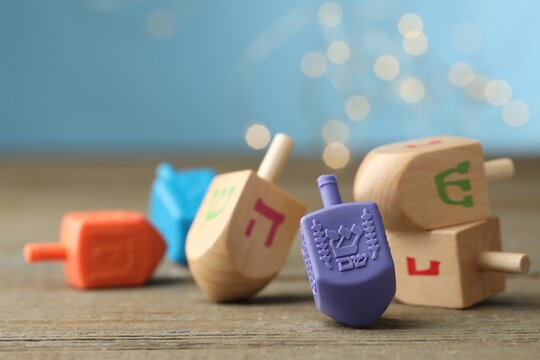 Hanukkah celebration. Dreidels with jewish letters on wooden table against light blue background with blurred lights, closeup. Space for text
