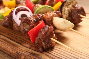 Delicious shish kebabs with vegetables on wooden table, closeup
