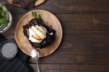 Tasty brownies served with ice cream and caramel sauce on wooden table, flat lay. Space for text