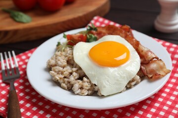 Tasty boiled oatmeal with fried egg, bacon and tomato served on table, closeup