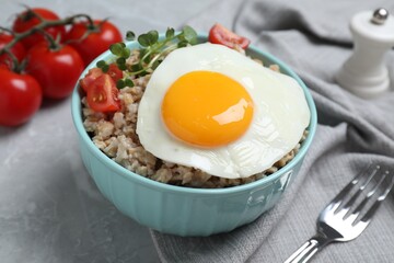 Tasty boiled oatmeal with fried egg, tomato and microgreens served on light grey table, closeup