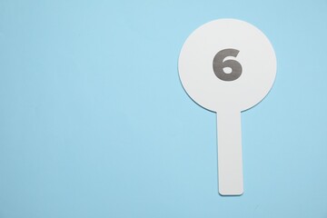 Auction paddle with number 6 on light blue background, top view. Space for text