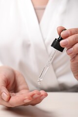Woman applying cosmetic serum onto fingers at white table, closeup