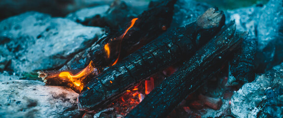 Vivid smoldered firewoods burned in fire close-up. Atmospheric warm background with orange flame of...