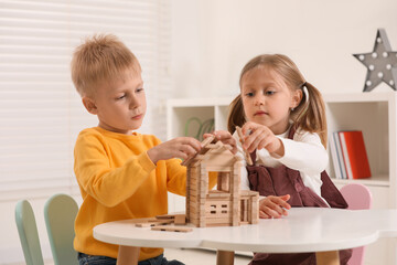 Obraz na płótnie Canvas Little boy and girl playing with wooden house at white table indoors. Children's toys