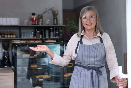 Happy business owner inviting to come into her cafe, space for text