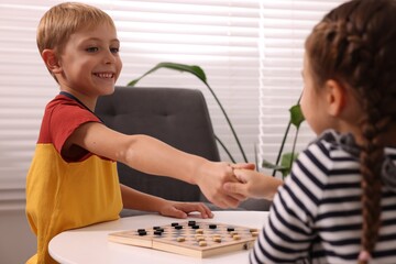 Children shaking hands after playing checkers at coffee table indoors