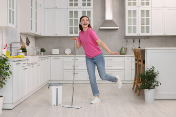 Enjoying cleaning. Happy woman in headphones dancing with mop in kitchen