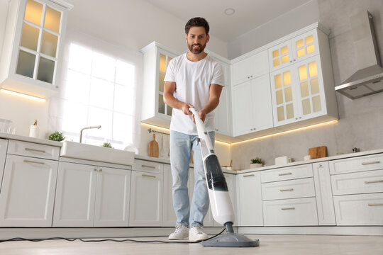 Happy man cleaning floor with steam mop in kitchen at home, low angle view