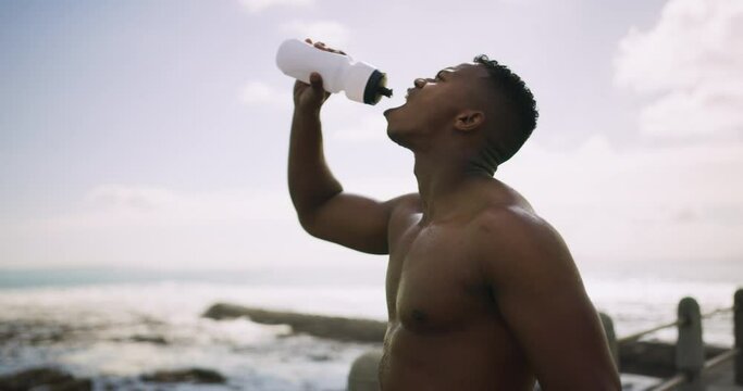 Break, fitness and a black man drinking water at the beach after running, cardio or exercise. Health, thirsty and an African runner or athlete with a bottle for a drink after training by the ocean