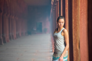 Naklejka premium A young woman with blond hair poses in a historical corridor with colorful columns, showing the beauty of architecture and fashion.
