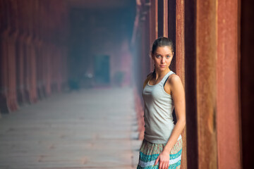 Naklejka premium A young woman with blond hair poses in a historical corridor with colorful columns, showing the beauty of architecture and fashion.