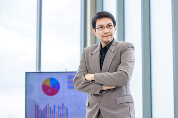 Millennial Asian professional successful male businessman entrepreneur boss leader in formal business suit outfit standing crossed arms posing in front of computer screen monitor in company office