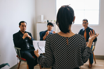 Back view of Asian businesswoman gives report or presentation to business colleagues in the...