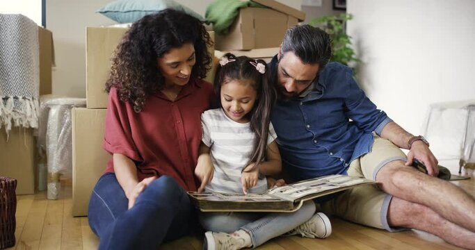 New home, parents and girl with a photo album, relax and boxes with property, loan and security in living room. Family, mother or father with a kid, childhood and development with memory and remember