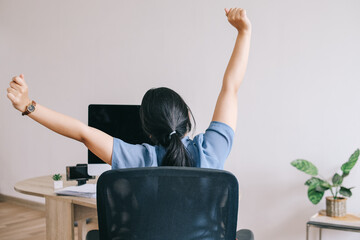 Back view of businesswoman warming up body and stretch her arms at workplace