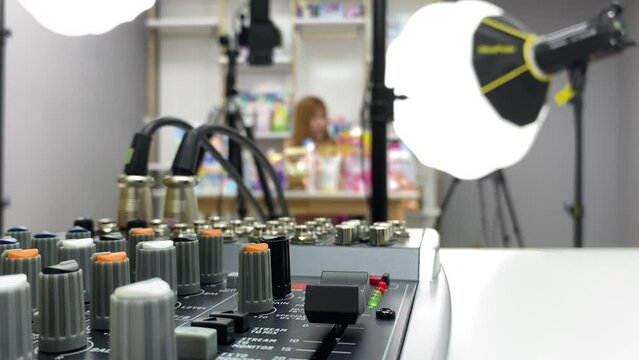 Audio equipment mixer console controller. Sound mixing tool on table inside studio close up view. Blurred live streamer female showing product to customers online.