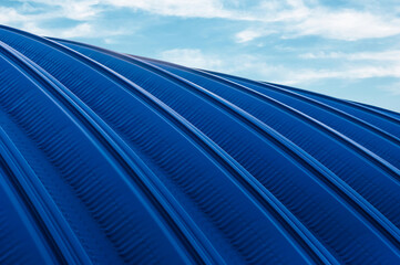The roof of a hangar made of blue rolled metal against the background of the sky with clouds. Metal...