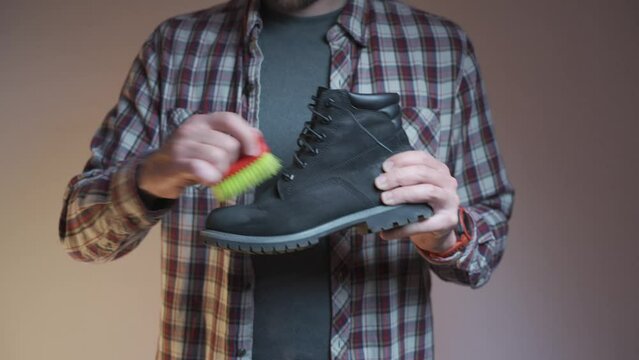 Topic care and brushing warm shoes expertly with small brush in workshop. Professional cleaning of nubuck shoes, suede autumn boots black, winter care and cleaning footwear. Boot maintenance studio. 