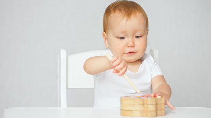Toddler girl plays with educational game for children sitting on high chair in light studio, close-up. Child development and childhood activities concept