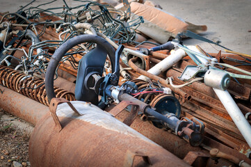 An old car steering wheel lies in a pile of rusty scrap metal. Car recycling concept.
