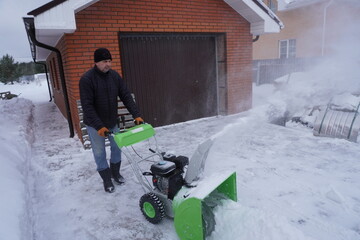 A man cleans snow in the winter in the courtyard of the house,  man cleaning snow with a snow blower