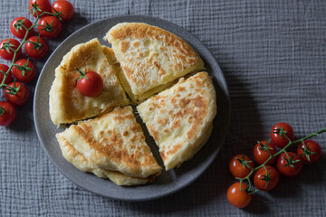Homemade cheese filled savoury pies khachapury on grey plate served with tomatoes. Selective focus