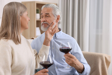 Affectionate senior couple with glasses of wine on sofa indoors