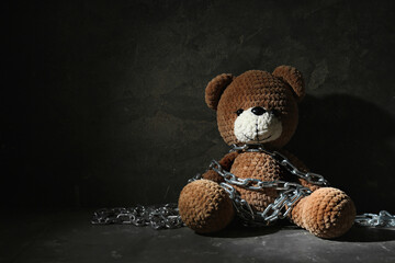 Stop child abuse. Chained toy bear in dark room. Space for text