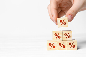 Woman building pyramid of cubes with percent signs on white background, closeup. Space for text