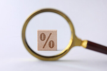 Cube with percent sign on white background, view through magnifying glass