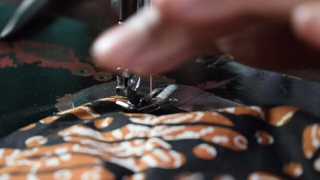 Close up Senior Female Tailor Sewing batik indonesian fabric into cloth, tailor hand, clothing, sewing machine, elder concept
