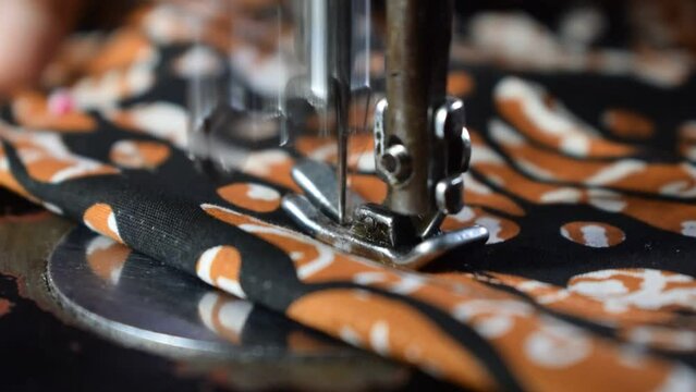 Close up Senior Female Tailor Sewing batik indonesian fabric into cloth, tailor hand, clothing, sewing machine, elder concept