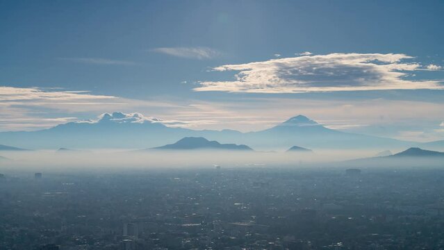 A high vantage point timelapse captures a breathtaking Mexico City valley sunrise, with the iconic active volcanoes Iztaccihuatl and Popocatepetl in the background. The smog and pollution are visible.