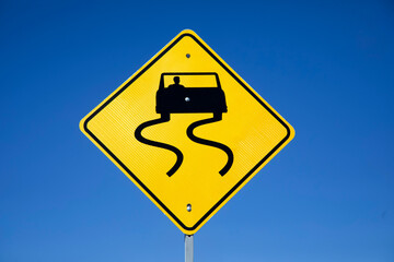 Yellow diamond shaped sign warning the road can be slippery.