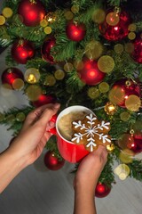 Closeup of hands gripping a red ceramic mug near a Christmas tree.