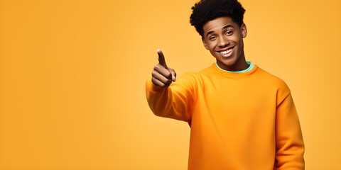 Happy funny African American teen guy pointing fingers to one side advertising new promo offer. Smiling black student model showing presenting ads standing isolated yellow background with copy space
